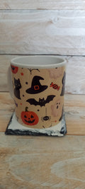 Halloween ceramic mug with cute icons including black cat, witch hat, bat, pumpkin, ghost and spider on cream background